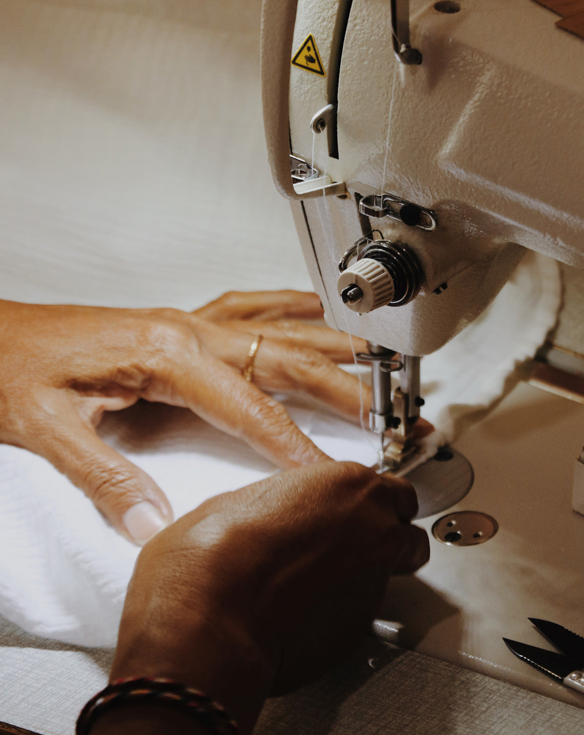 Close-up of hands stitching a white dress, holding white cotton fabric on the sewing machine.