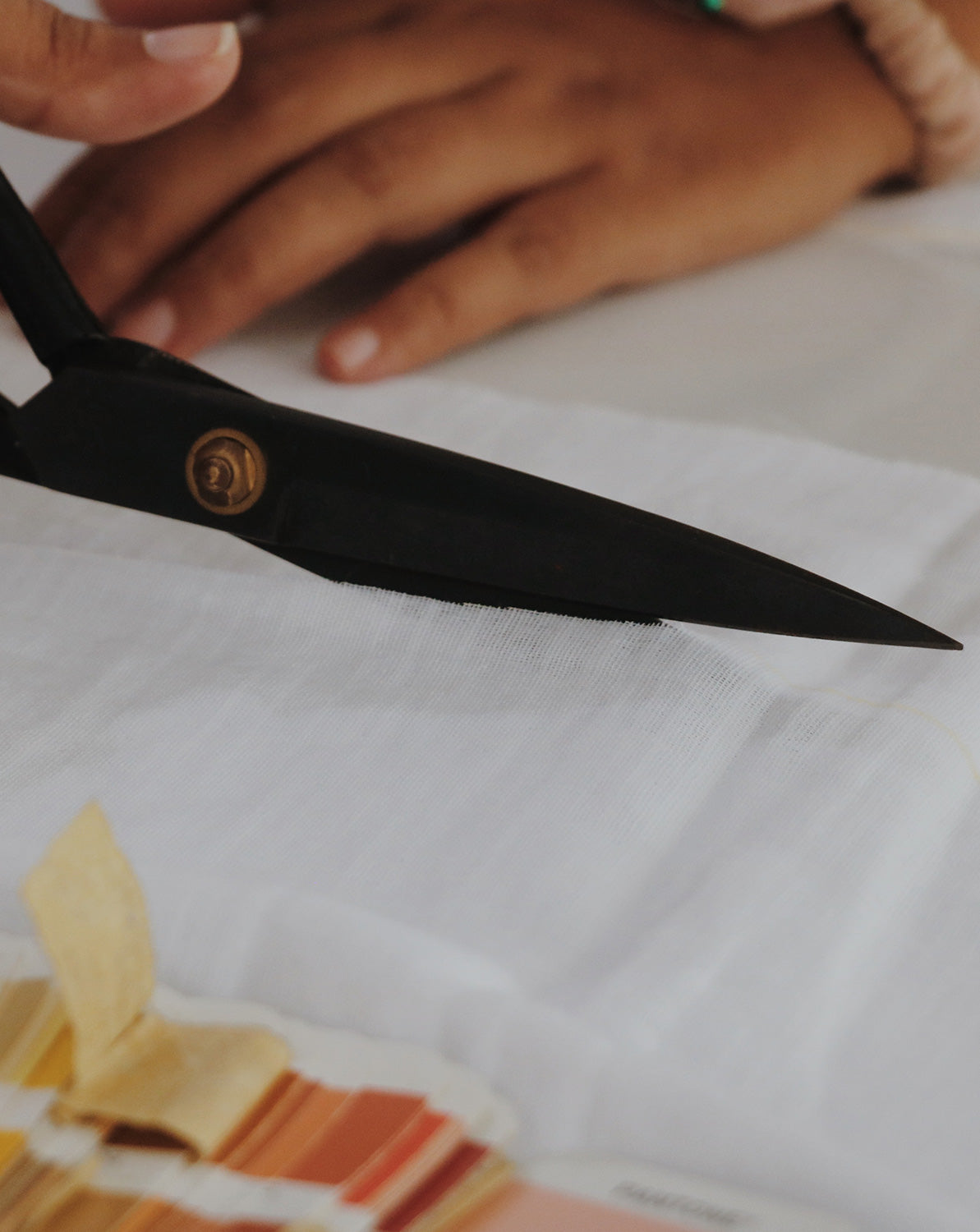 Close-up of a pair of tailor scissors cutting a piece of white cotton fabric to make a dress.