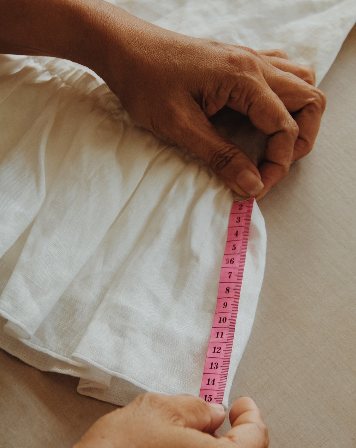 Close-up of two hands quality checking and measuring the length of a dress using a measuring tape.