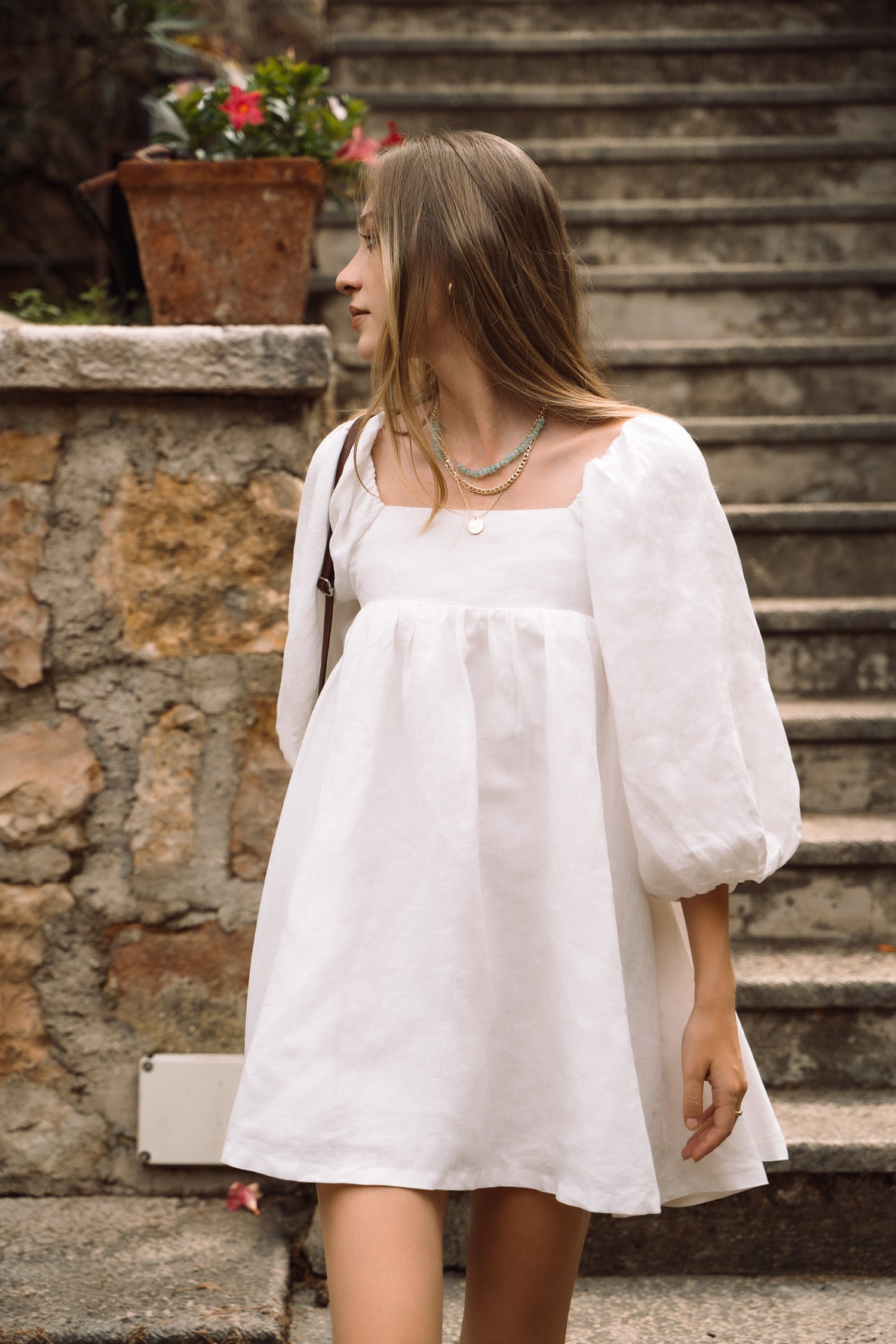 A white linen mini dress, with puff sleeves, straight neckline and open back with bow ties.