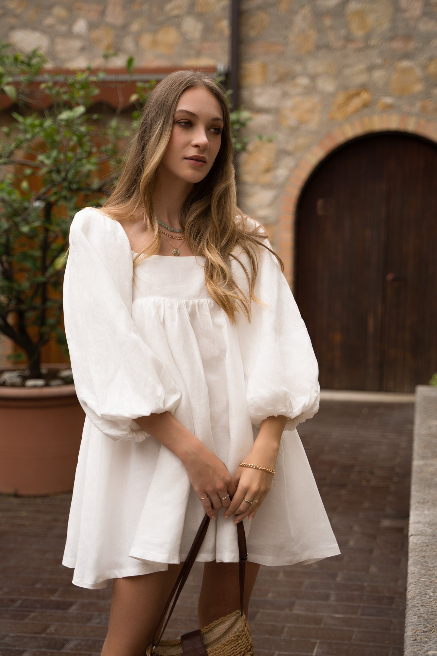 A white linen mini dress, with puff sleeves, straight neckline and open back with bow ties.