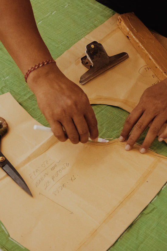 Close-up of hands drafting a paper pattern on a piece of green cotton fabric in preparation of sewing the dress.