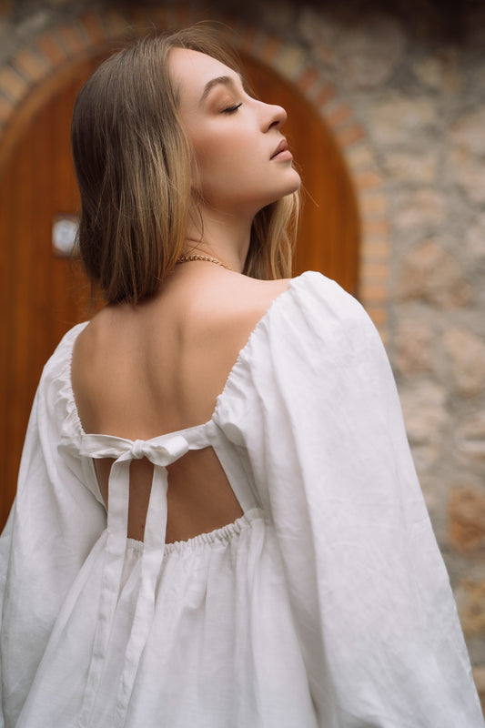 A white linen mini dress, with puff sleeves, straight neckline and open back with bow ties.