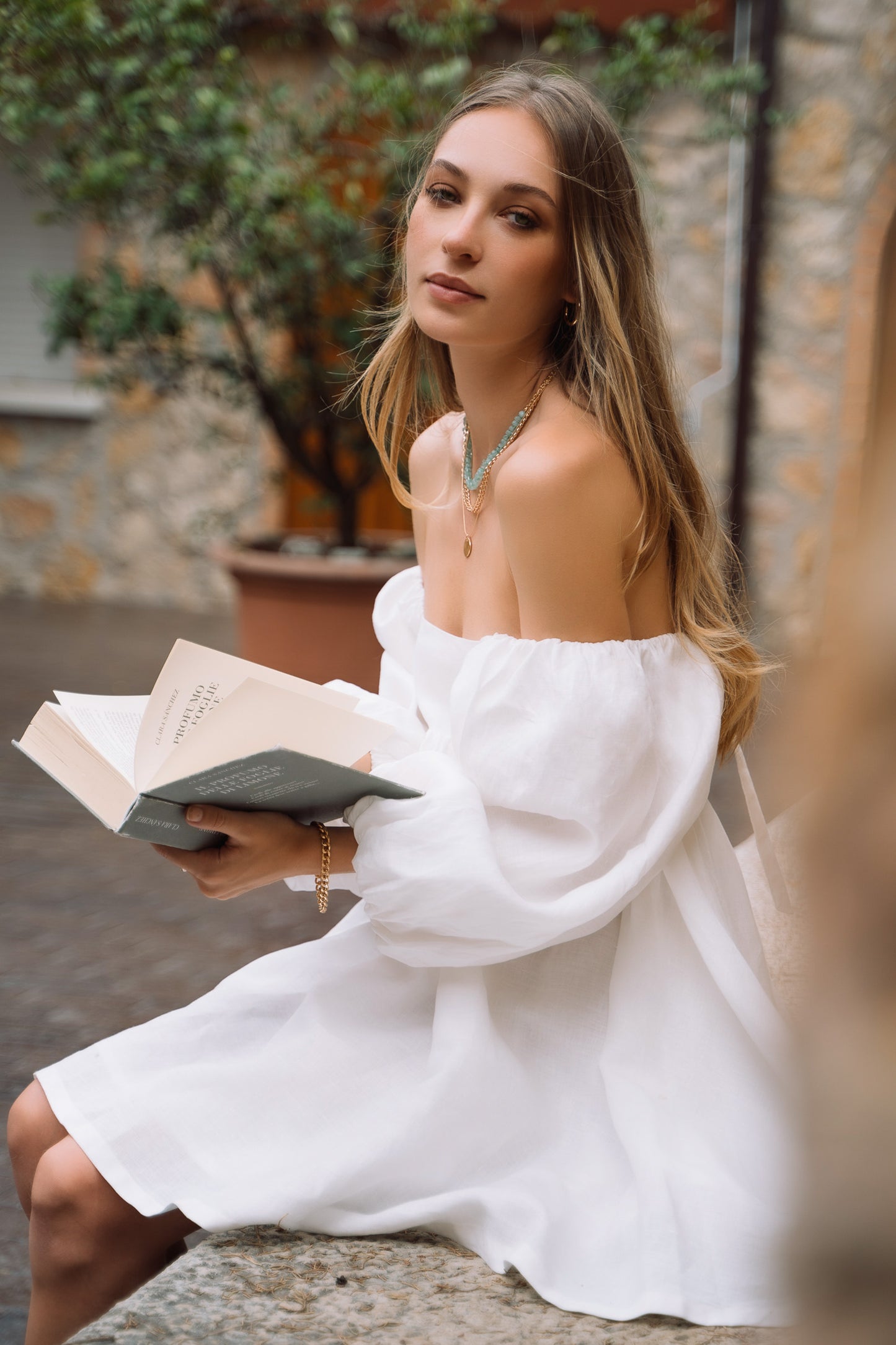 A white linen mini dress, with off-shoulders puff sleeves, straight neckline and open back with bow ties.