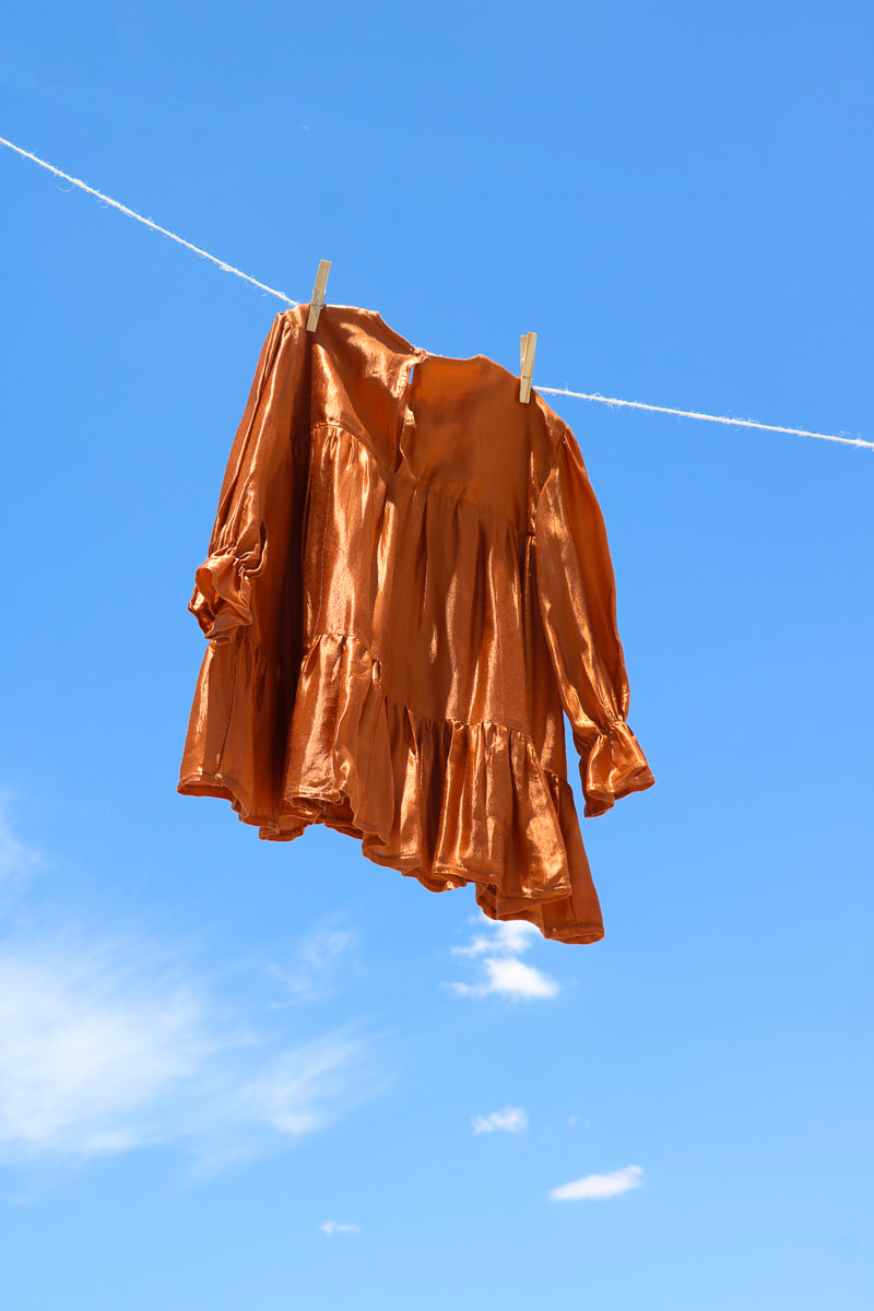 Back of orange shiny bemberg cupro dress for girls, with long sleeves and tiered skirt.