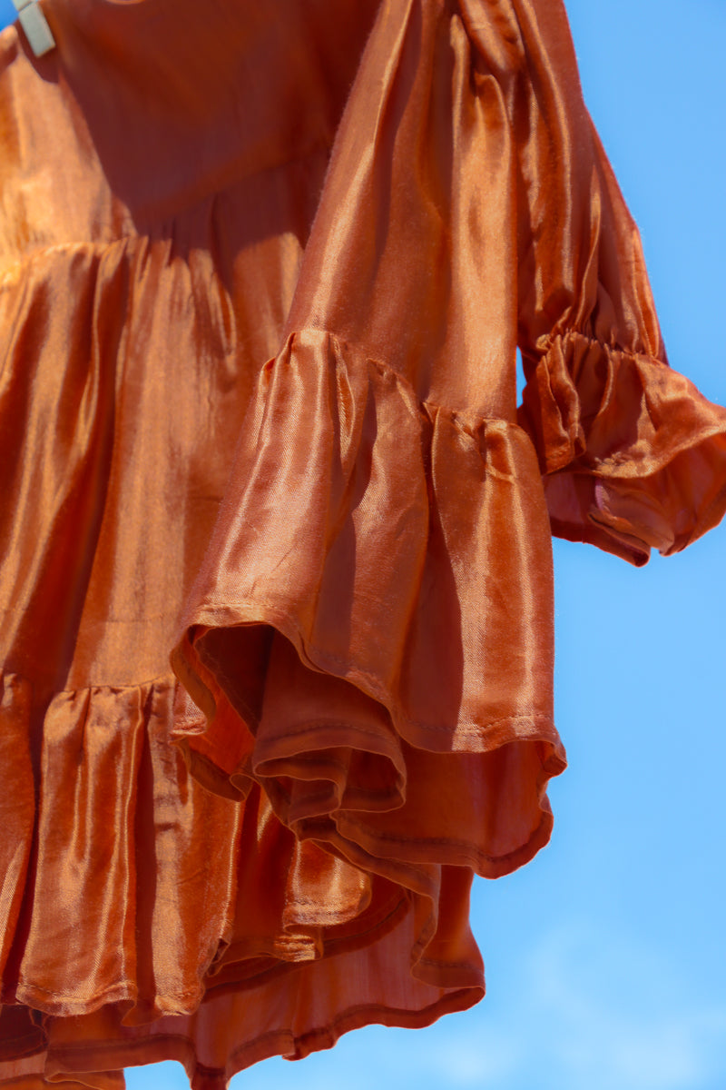 Close-up orange girls dress, with long sleeves, frilled wrist cuffs and tiered skirt.