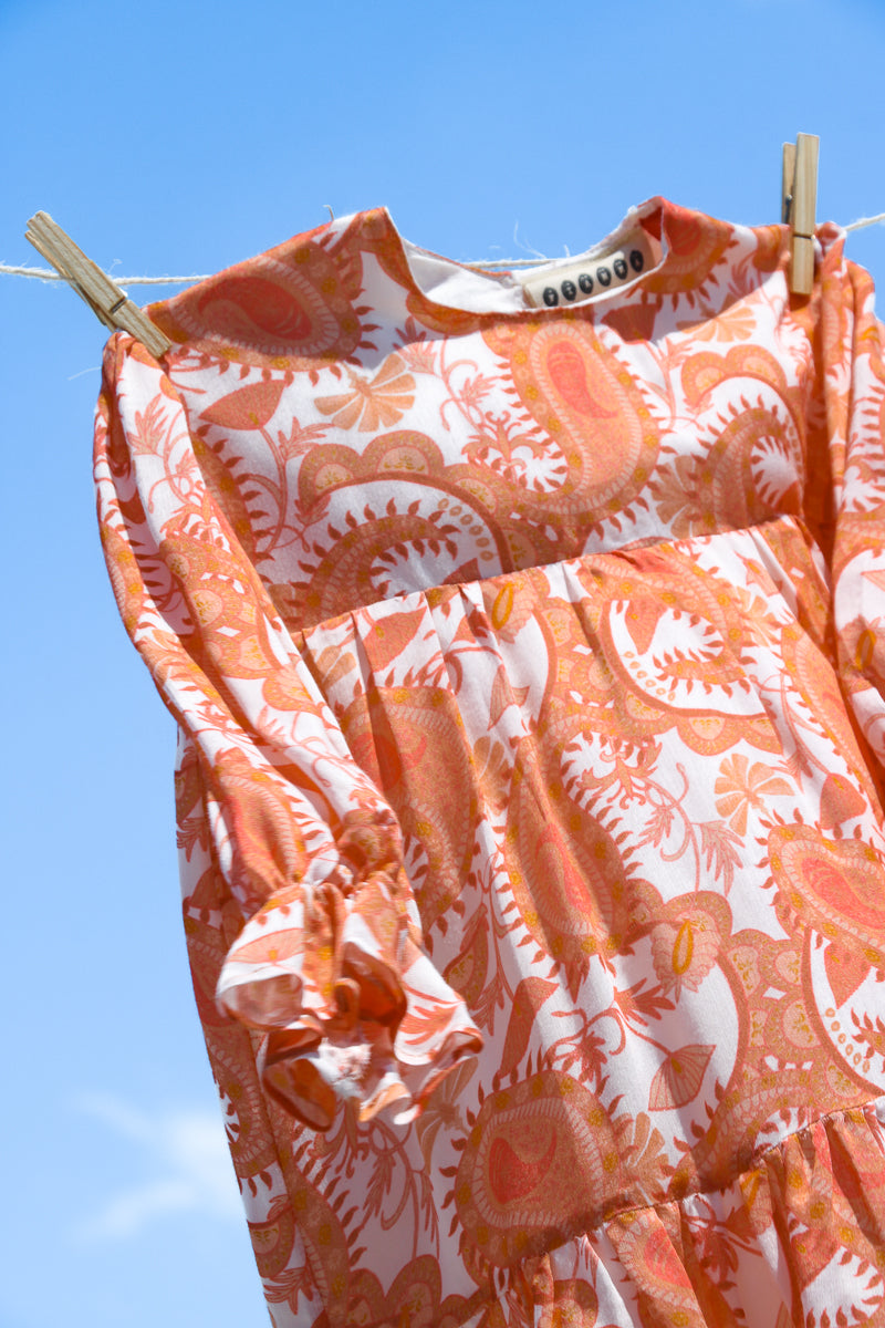 Close-up of sustainable and ethical dress for girls, in bemberg cupro shiny fabric, printed with orange paisleys pattern. Matching mum and daughter dress.