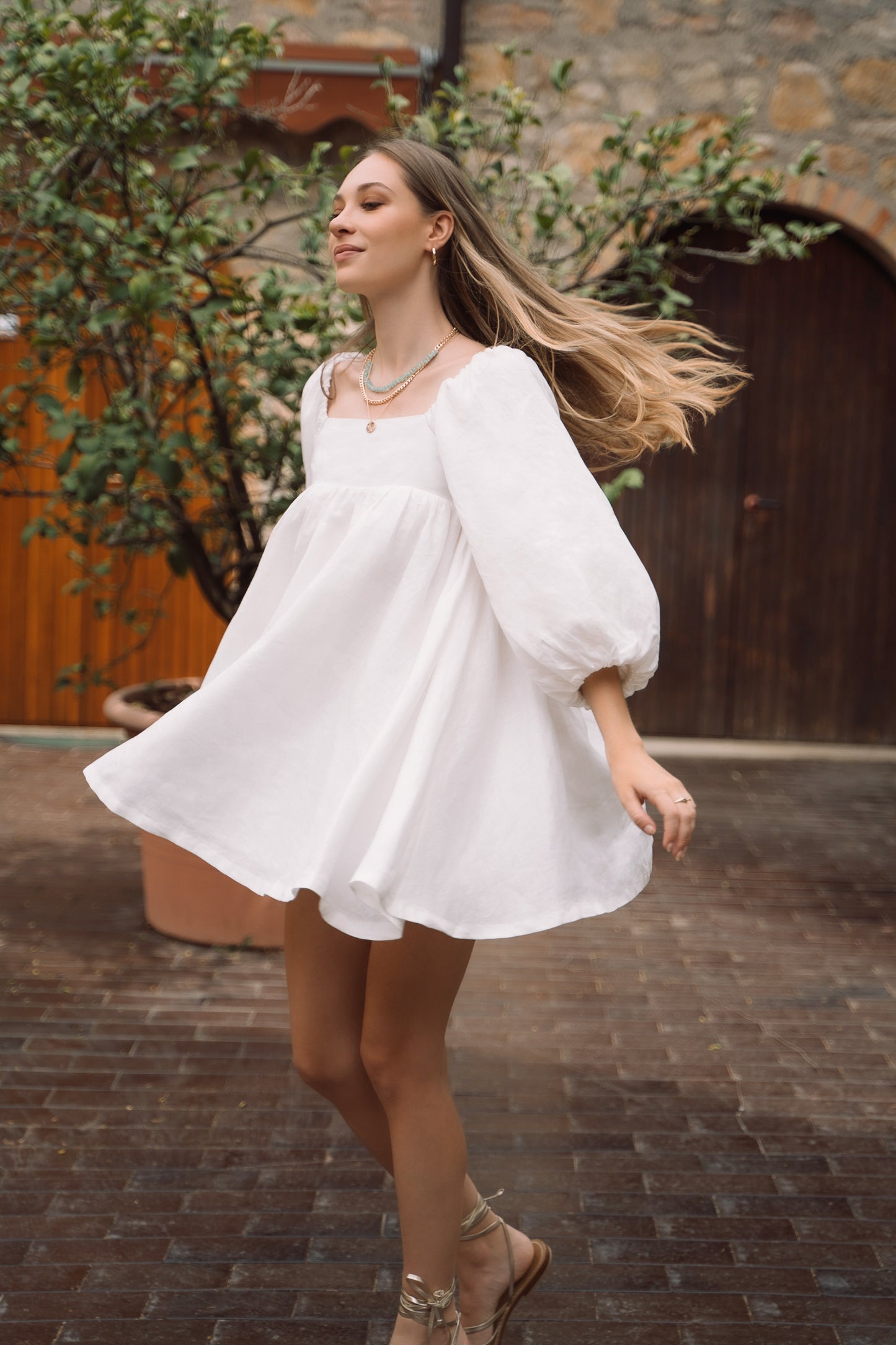 Woman spinning wearing white sustainable linen mini dress, with puff sleeves and voluminous skirt.